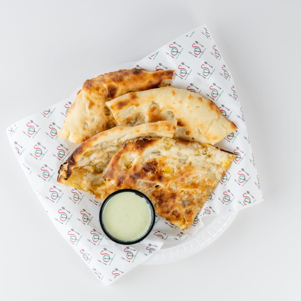 Stacked golden-brown stuffed flatbreads served with creamy dipping sauce on branded paper.
