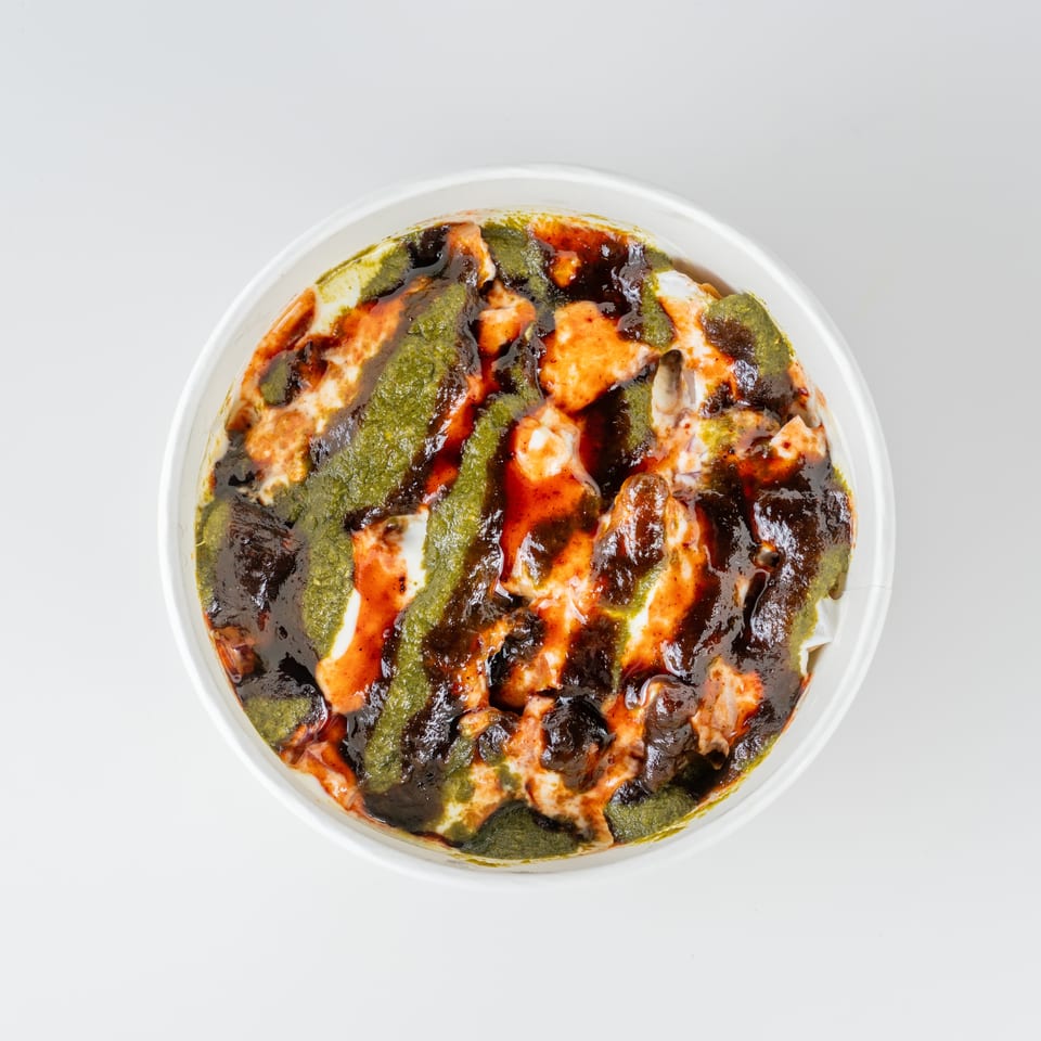 Top-down view of creamy Indian chaat topped with green chutney, tamarind sauce, and red chili sauce in a white bowl.
