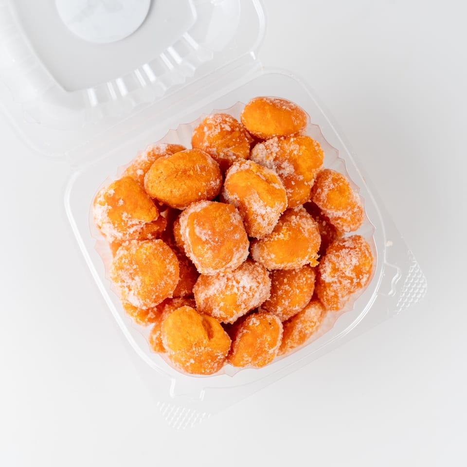 Clear container filled with golden fried dough bites coated in coarse sugar.