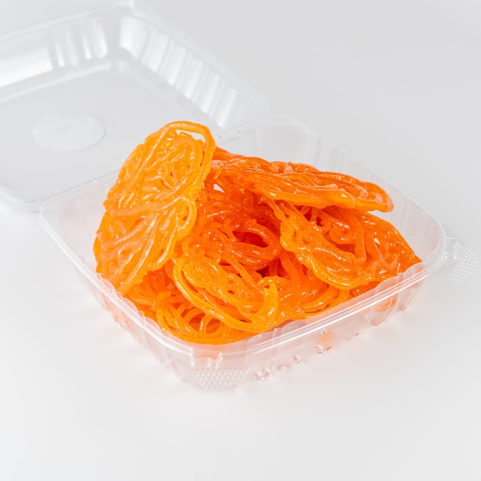 Bright orange jalebi sweets piled in a clear takeaway container.