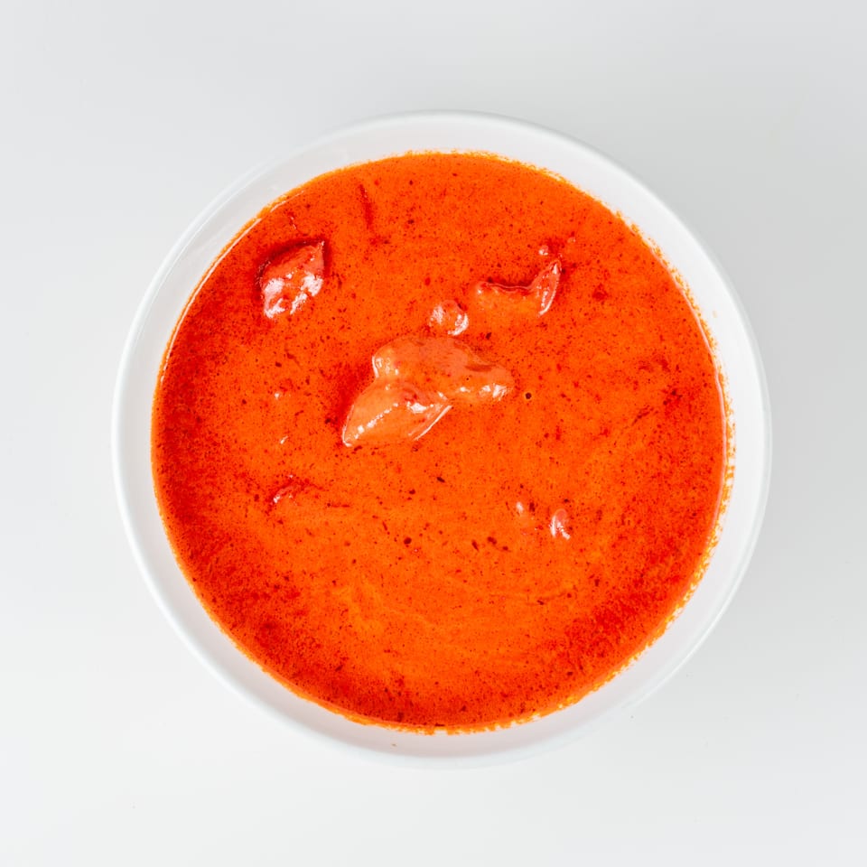 Bowl of creamy orange curry with several pieces of chicken, photographed from above on a white background.