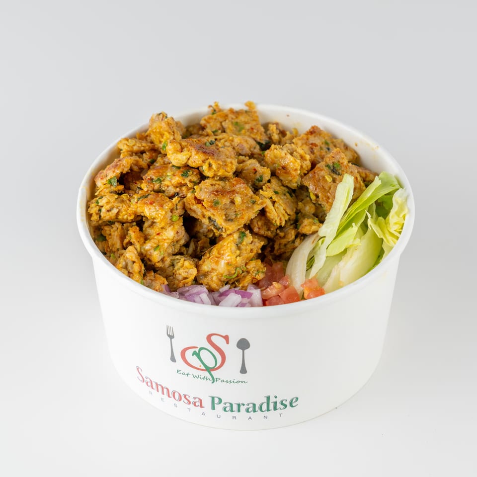 A bowl of crispy golden samosas with lettuce, tomatoes, and red onions in a Samosa Paradise container.