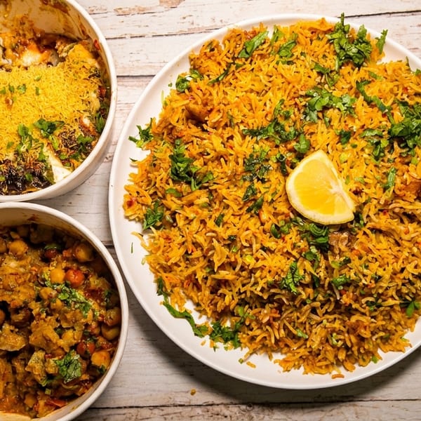 A large plate of biryani with a lemon wedge, a bowl of sev puri, and a bowl of chana masala.